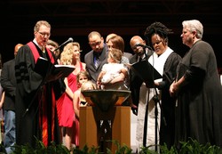 Photo of a group of people gathered around a baptismal font as a baby is baptized