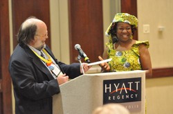 Photo of a man and woman standing behind a podium; the man is handing an envelope to the woman