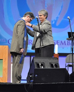 Photo of a woman placing a liturgical stole on the shoulders of a man