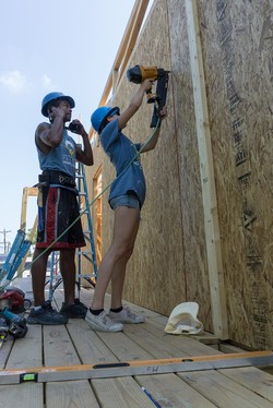 Workforce development member, Aaron Franklin-White, and French volunteer, Claire, complete the exterior of a newly constructed home.