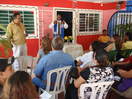 The Rev. Byron Wade speaks to a group of people in front of a red  building with white windows