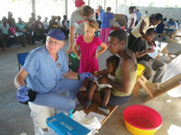 A doctor attends to a woman and her young child, with a girl standing beside him.