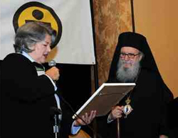 A woman hands a man in vestments and a robe a plaque.