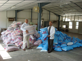 Two men in front of piles of blue and translucent colored pillow and sheet sets, each holding one.