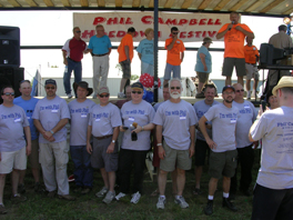 A group of people in grey shirts standing below a stage, with others standing on it.