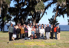 A group of men and women, standing under a tree poised for a photo.