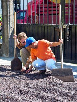 Two men stooping in gravel, holding shovels.