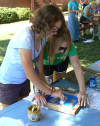 Two young women screen pressing paint over a t-shirt.