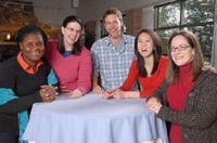 A  group of people around a small round table with a periwinkle  tablecloth.