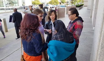 Cindy Kohlmann huddles in prayer with one family ahead of their monthly appointment with ICE officials.