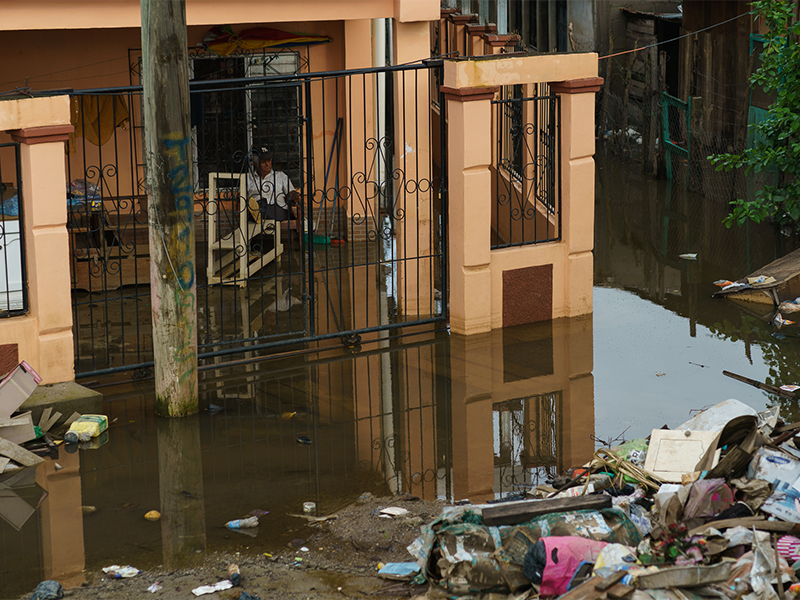 A man sits on a raised chair in his flooded home in La Lima, Honduras. Photo by Gregg Brekke. 